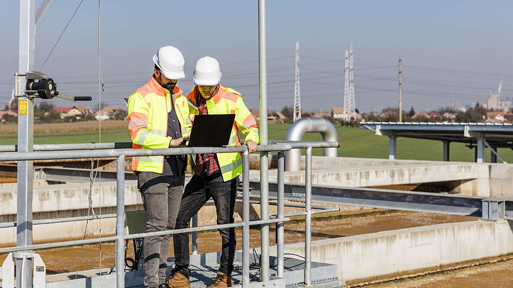 Two wastewater treatment plant operators using a laptop to review plant data