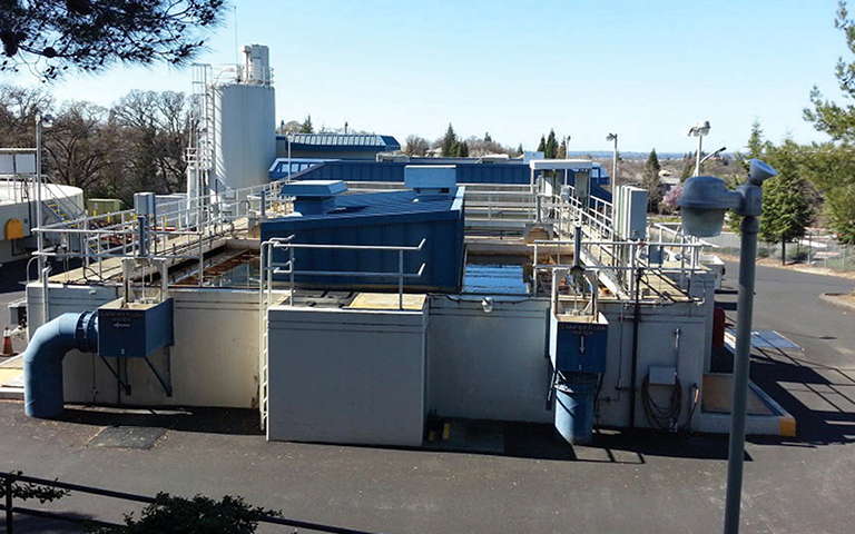 Trident-Adsorption Clarifier installation. It is a large, open, rectangular concrete structure flanked by railed walkways, with control panels at the left.