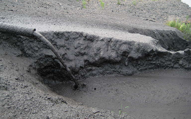 Encrusted drain pipe dispelling thickened tailings into a mud-filled deposition site